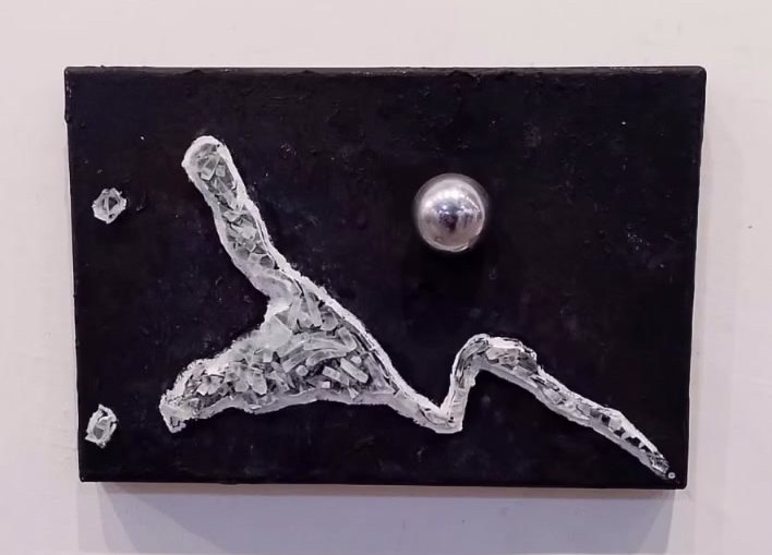 Placa negra con una figura blanca de brazos abiertos y una esfera de metal plateada